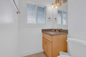 Half bath with baseboards, toilet, a healthy amount of sunlight, and vanity