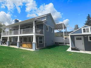 Back of property featuring a hot tub, board and batten siding, a balcony, a yard, and a patio