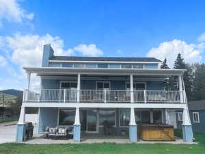 Back of house featuring a hot tub, a balcony, a patio area, and a chimney