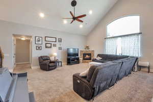 Living room featuring high vaulted ceiling, a tile fireplace, light carpet, baseboards, and ceiling fan