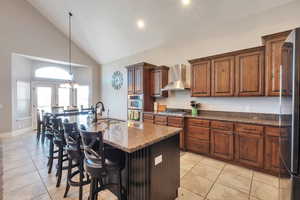 Kitchen featuring wall chimney exhaust hood, appliances with stainless steel finishes, a sink, a kitchen breakfast bar, and light tile patterned floors