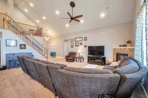 Living room featuring carpet flooring, high vaulted ceiling, stairs, a fireplace, and ceiling fan