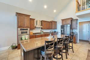 Kitchen featuring a sink, wall chimney range hood, stainless steel appliances, and light tile patterned flooring