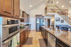 Kitchen with wall chimney range hood, stone counters, a sink, and stainless steel appliances