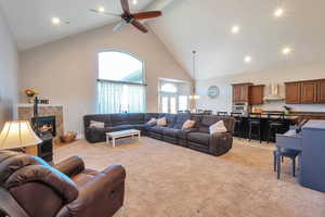 Living area with high vaulted ceiling, a tiled fireplace, a ceiling fan, and light carpet