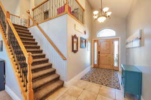 Entrance foyer with stairs, high vaulted ceiling, a chandelier, light tile patterned floors, and baseboards