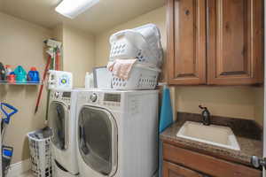 Laundry area featuring separate washer and dryer, cabinet space, and a sink