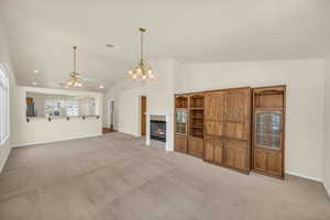 Unfurnished living room featuring lofted ceiling, a chandelier, ceiling fan, a fireplace, and light carpet