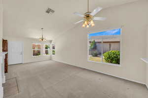 Unfurnished living room featuring lofted ceiling, carpet flooring, a chandelier, and a ceiling fan