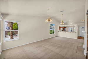 Unfurnished living room with lofted ceiling, light colored carpet, ceiling fan, a chandelier, and a textured ceiling