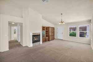 Unfurnished living room with light carpet, plenty of natural light, a tile fireplace, a chandelier, and high vaulted ceiling