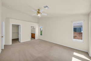 Unfurnished bedroom featuring light carpet, a spacious closet, a closet, ensuite bathroom, and lofted ceiling