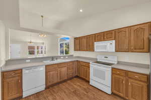 Kitchen with white appliances, a chandelier, vaulted ceiling, brown cabinets, and wood finished floors
