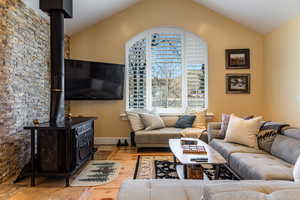 Living room with baseboards, lofted ceiling, wood finished floors, and a wood stove