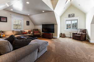 Carpeted living area featuring a wealth of natural light, vaulted ceiling, and baseboards