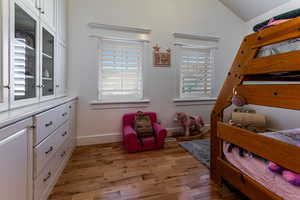 Bedroom featuring baseboards, lofted ceiling, and light wood-style flooring