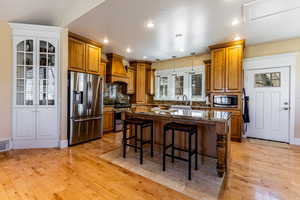 Kitchen with light wood-type flooring, stainless steel appliances, a breakfast bar, brown cabinetry, and custom exhaust hood