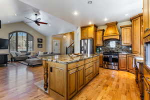 Kitchen with a kitchen island, ceiling fan, appliances with stainless steel finishes, custom exhaust hood, and brown cabinets