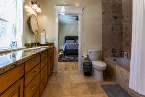 Bathroom with connected bathroom, toilet, a ceiling fan, vanity, and tiled shower / bath