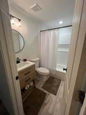 Bathroom featuring shower / bath combination with curtain, wood finished floors, visible vents, toilet, and vanity