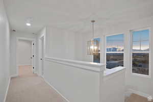 Hallway featuring an inviting chandelier, baseboards, light colored carpet, and visible vents