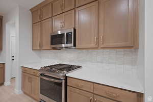 Kitchen with baseboards, light countertops, backsplash, and appliances with stainless steel finishes