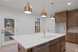 Kitchen featuring light countertops, tasteful backsplash, stainless steel dishwasher, a sink, and light wood-style flooring