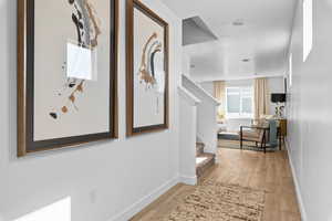 Hallway with light wood finished floors, stairs, and baseboards
