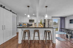 Kitchen featuring a breakfast bar, white cabinets, stainless steel appliances, and dark countertops
