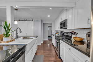 Kitchen featuring stainless steel appliances, dark wood finished floors, decorative backsplash, a sink, and white cabinets