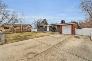 Ranch-style home featuring fence, a chimney, a garage, brick siding, and a front lawn