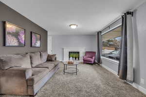 Carpeted living room featuring baseboards, a textured ceiling, and a brick fireplace