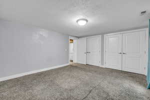 Unfurnished bedroom featuring carpet floors, a textured ceiling, baseboards, visible vents, and two closets