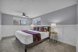Carpeted bedroom featuring a decorative wall, multiple windows, and ceiling fan
