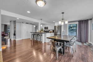 Dining space with a textured ceiling, baseboards, recessed lighting, a barn door, and dark wood-style floors