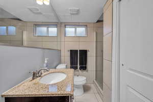 Bathroom featuring tile patterned floors, toilet, vanity, a shower stall, and tile walls
