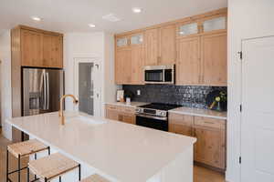 Kitchen with decorative backsplash, stainless steel appliances, glass insert cabinets, a sink, and a kitchen breakfast bar