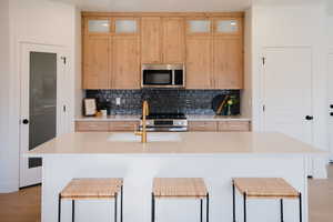Kitchen featuring a kitchen island with sink, light countertops, backsplash, and stainless steel appliances