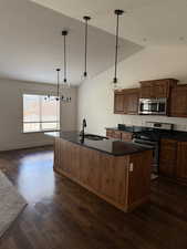 Kitchen featuring appliances with stainless steel finishes, dark wood-style floors, a kitchen island with sink, and dark countertops