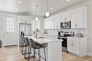 Kitchen featuring light wood finished floors, a kitchen island with sink, stainless steel appliances, a sink, and a kitchen breakfast bar