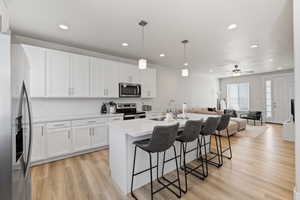 Kitchen featuring a breakfast bar, appliances with stainless steel finishes, white cabinetry, a sink, and open floor plan