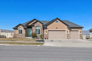 View of front of house with stone siding, driveway, fence, a garage, and stucco siding