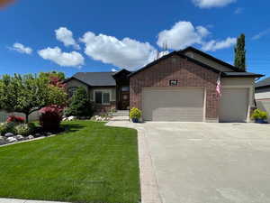Single story home featuring an attached garage, a front lawn, concrete driveway, and brick siding