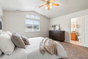 Bedroom with lofted ceiling, visible vents, ensuite bath, light colored carpet, and ceiling fan