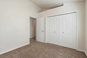 Unfurnished bedroom with baseboards, vaulted ceiling, a closet, and carpet