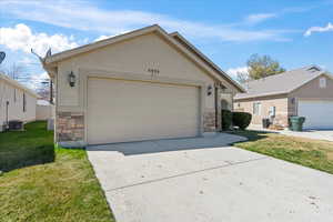 Ranch-style home featuring stucco siding, driveway, stone siding, a front yard, and a garage