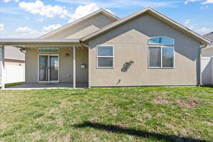 Rear view of house featuring stucco siding, fence, a patio area, and a yard