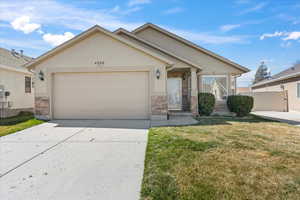 Ranch-style home with a front lawn, stone siding, concrete driveway, an attached garage, and stucco siding