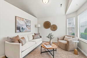Carpeted living area featuring lofted ceiling, baseboards, and visible vents