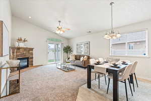 Dining area featuring light carpet, baseboards, ceiling fan with notable chandelier, lofted ceiling, and a stone fireplace